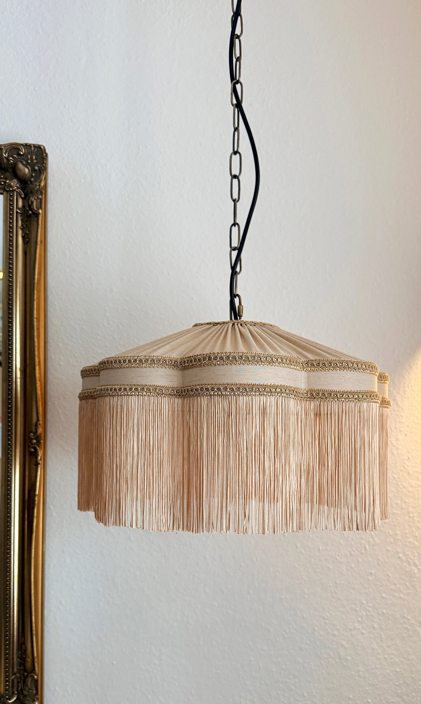 Beige pendant light with fringe detail hanging against a white wall. The House of Soft Light
