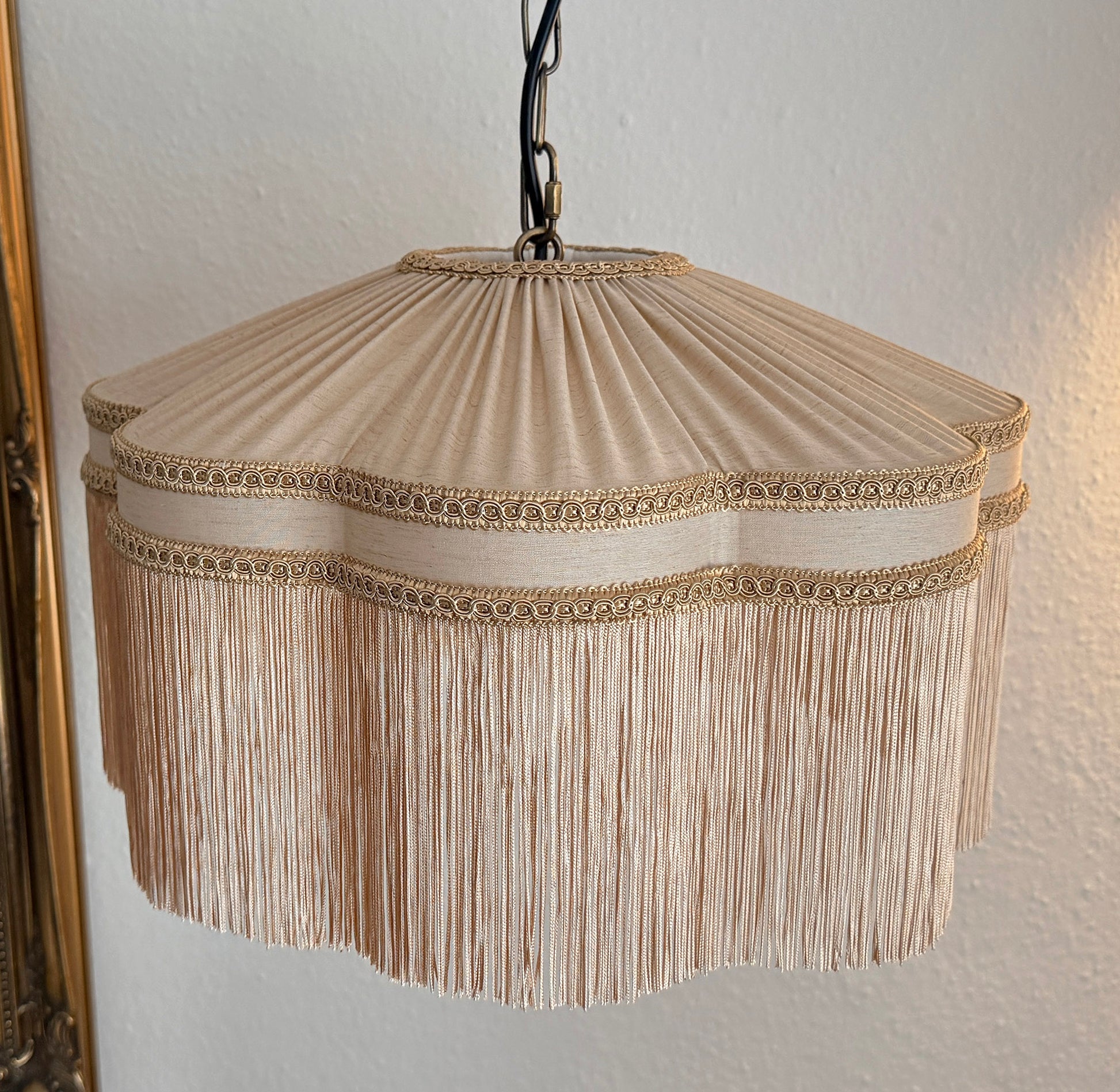 Beige pleated lampshade with fringe details on a plain wall.