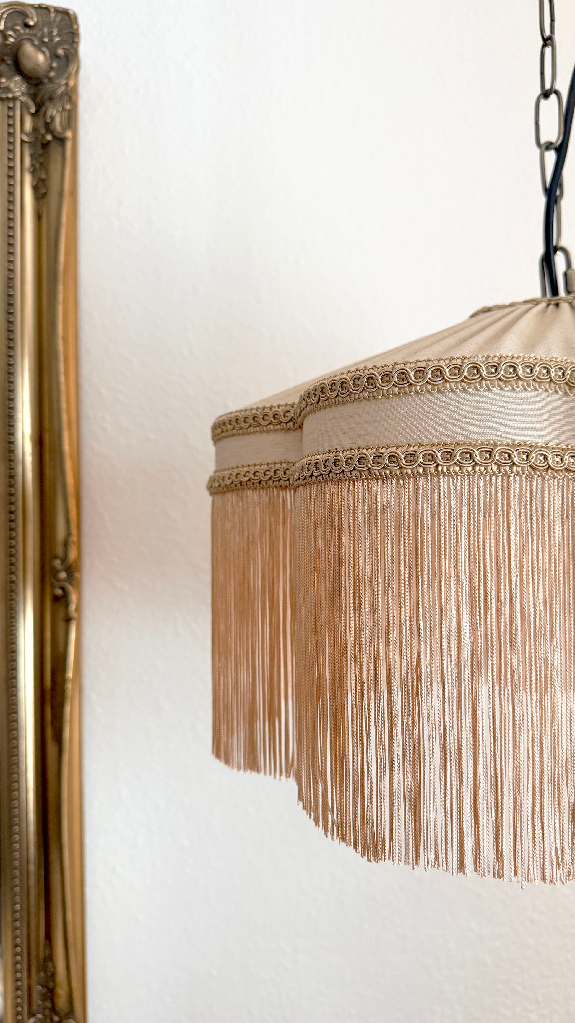 Decorative lamp with fringe detail hanging against a white wall.
