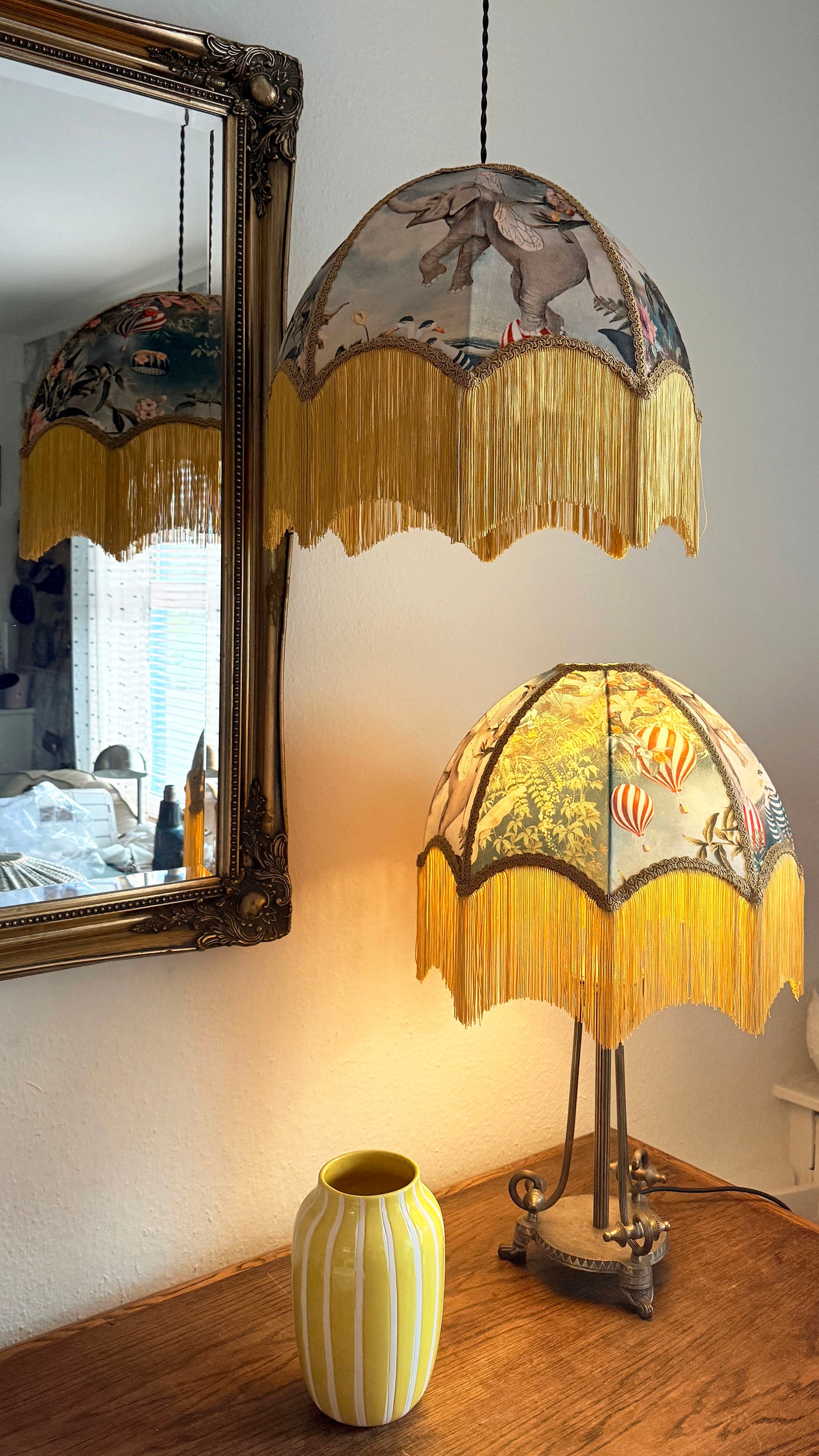 Decorative lamp with fringed shade on a wooden surface, mirror reflecting room interior.