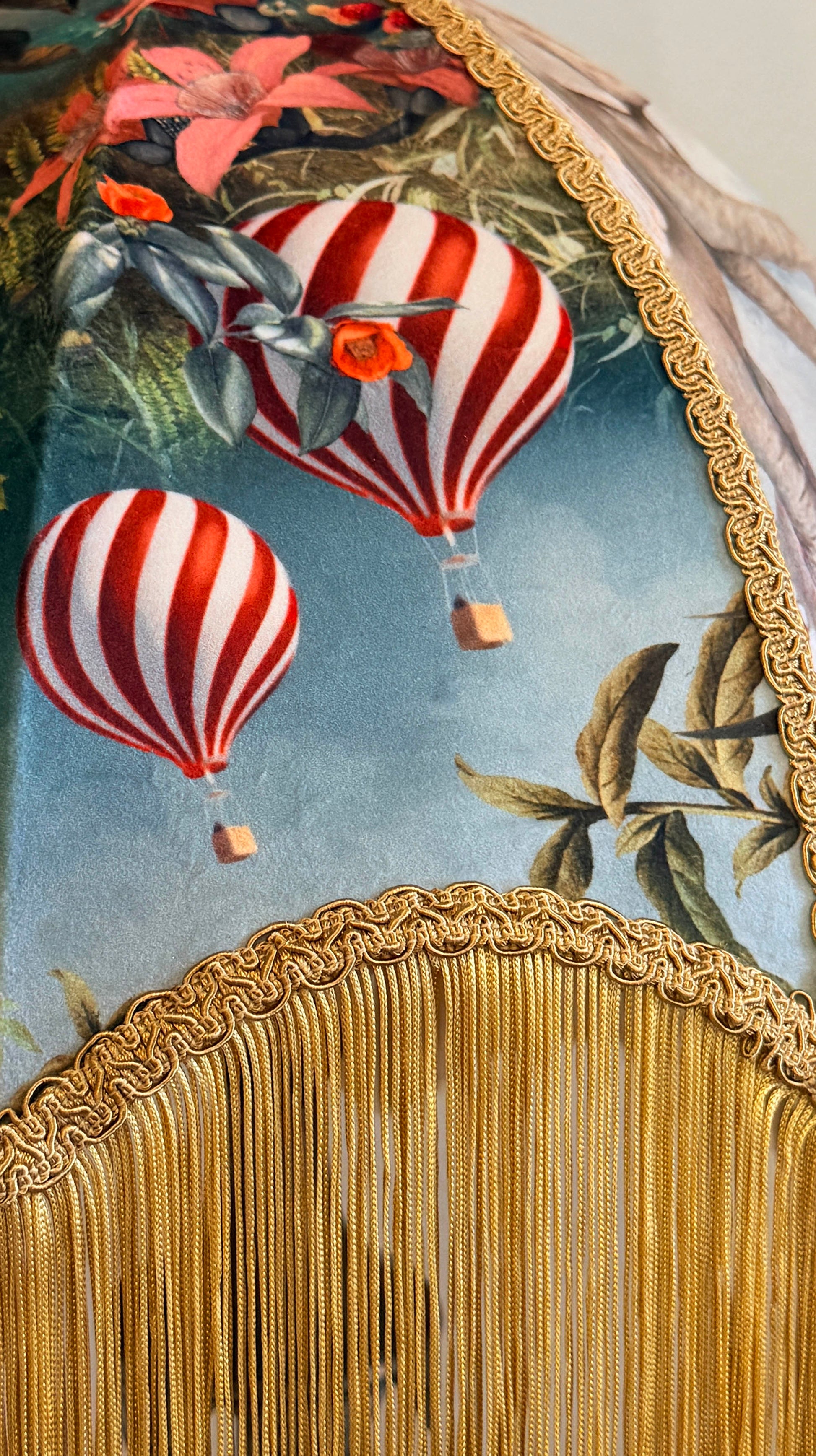 Decorative fabric lampshade with hot air balloons and floral elements, featuring a gold fringe at the bottom.