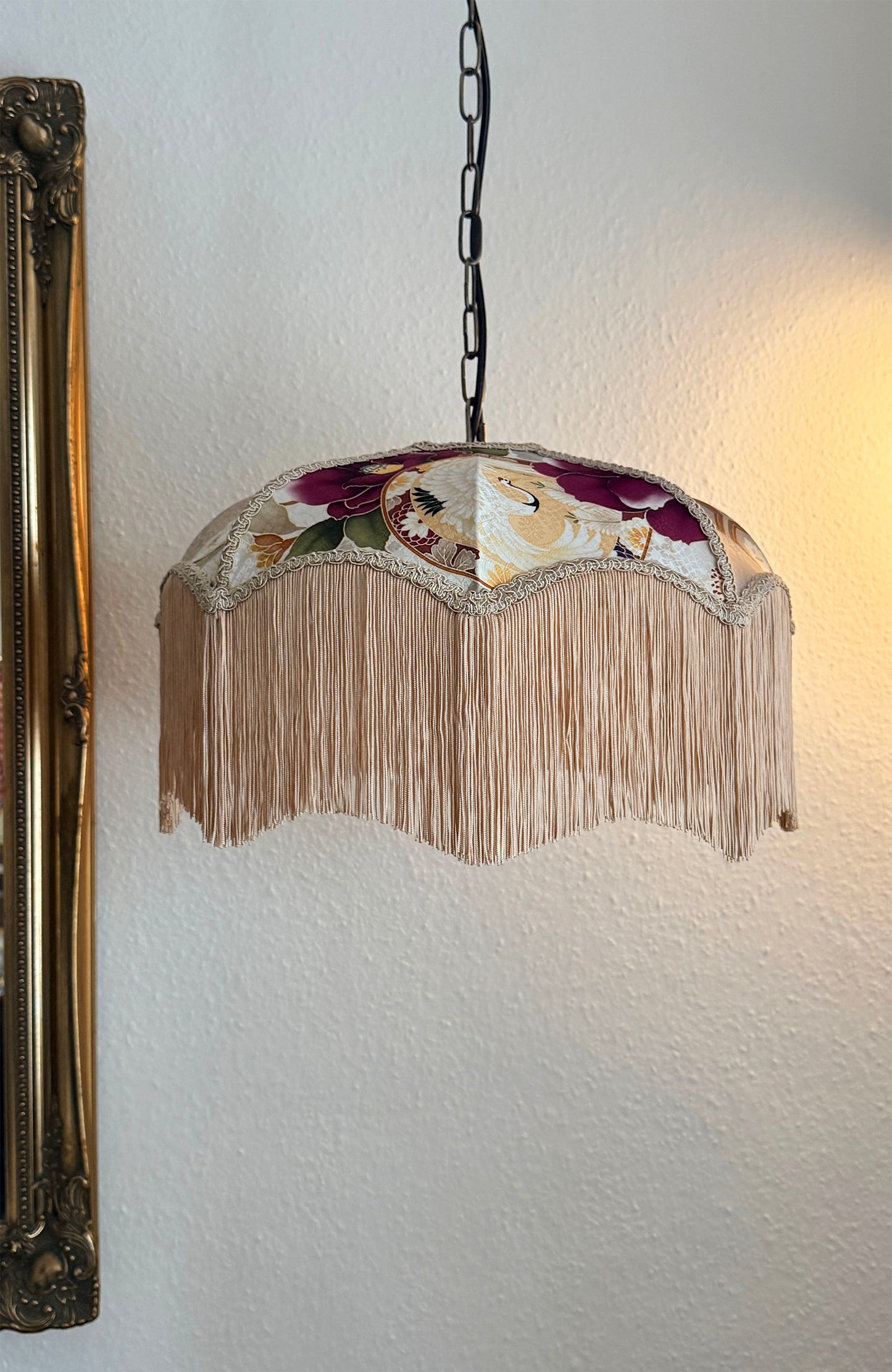 Decorative lamp with floral design and fringe on a white wall.