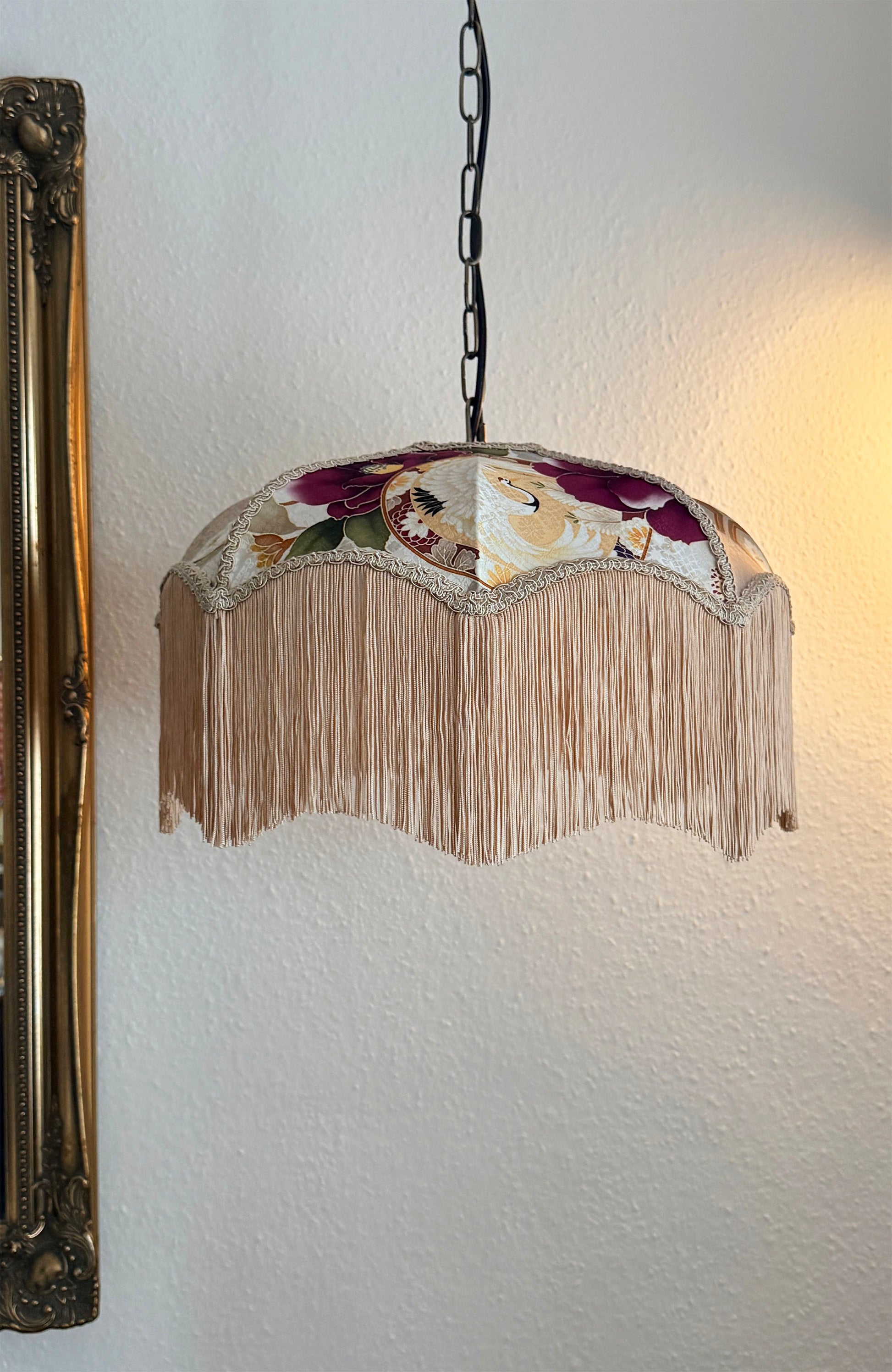 Decorative lamp with floral design and fringe on a white wall.