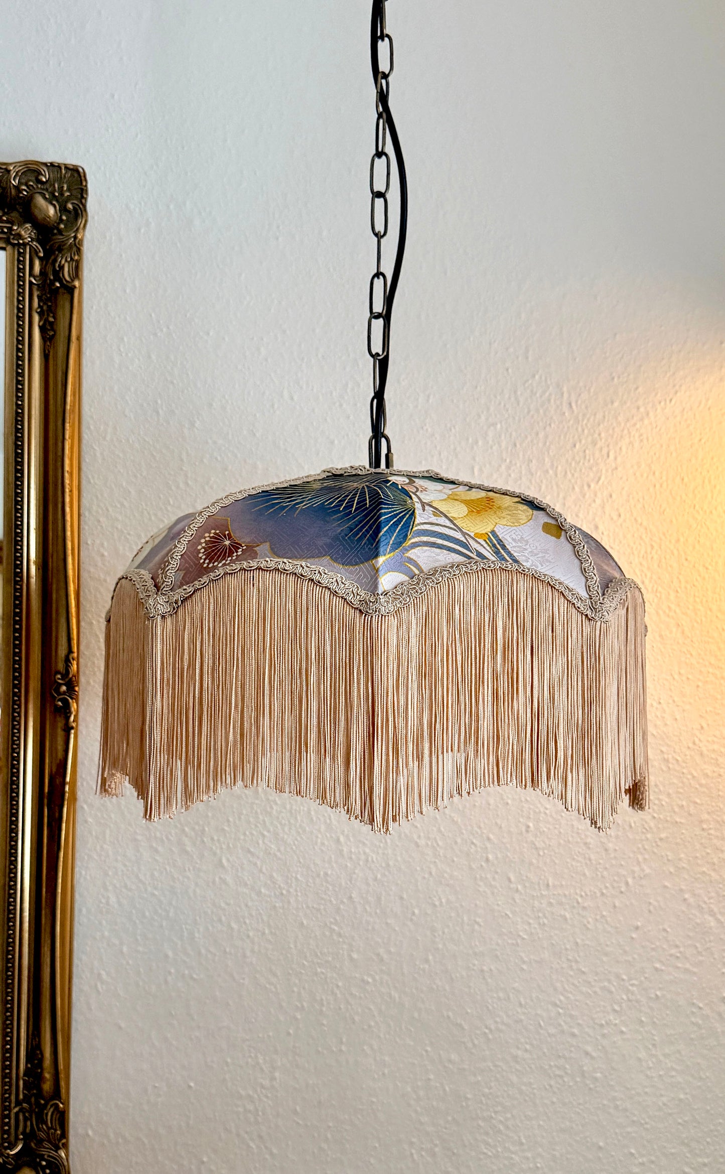 Decorative pendant light with floral silk design and fringe on a white wall. The House of Soft Light