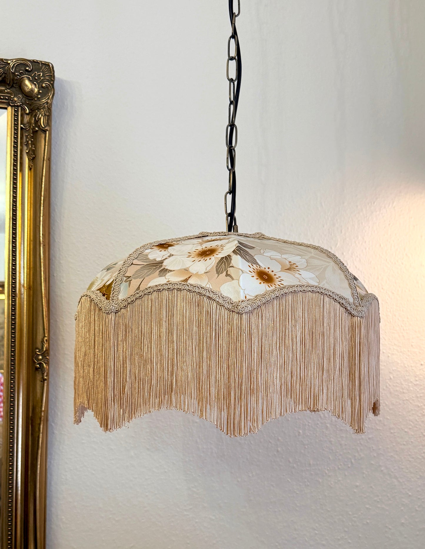 Decorative pendant light with floral design and fringe on a white wall. The House of Soft Light