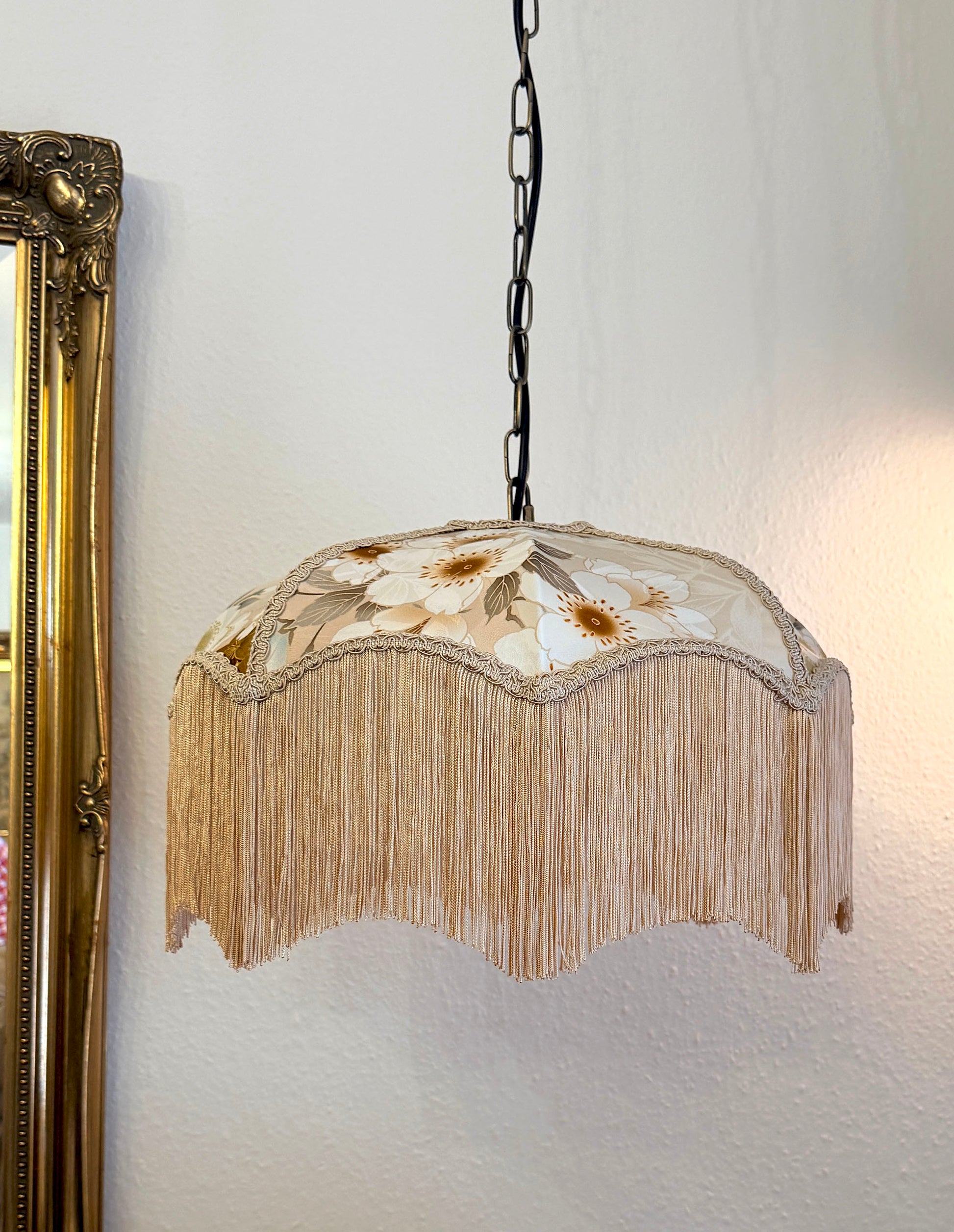 Decorative pendant light with floral design and fringe on a white wall. The House of Soft Light