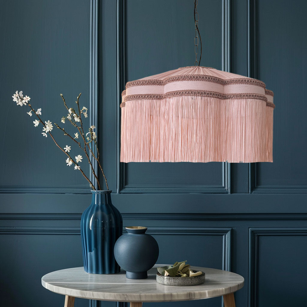 Pink pendant lamp hanging above a table with decorative vases and branches against a dark blue paneled wall.