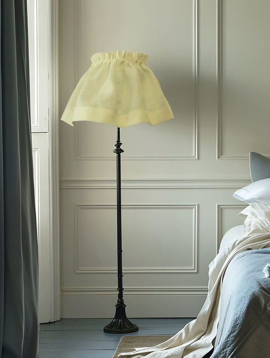 Floor lamp with a light green shade in a room with panelled walls and a bed.