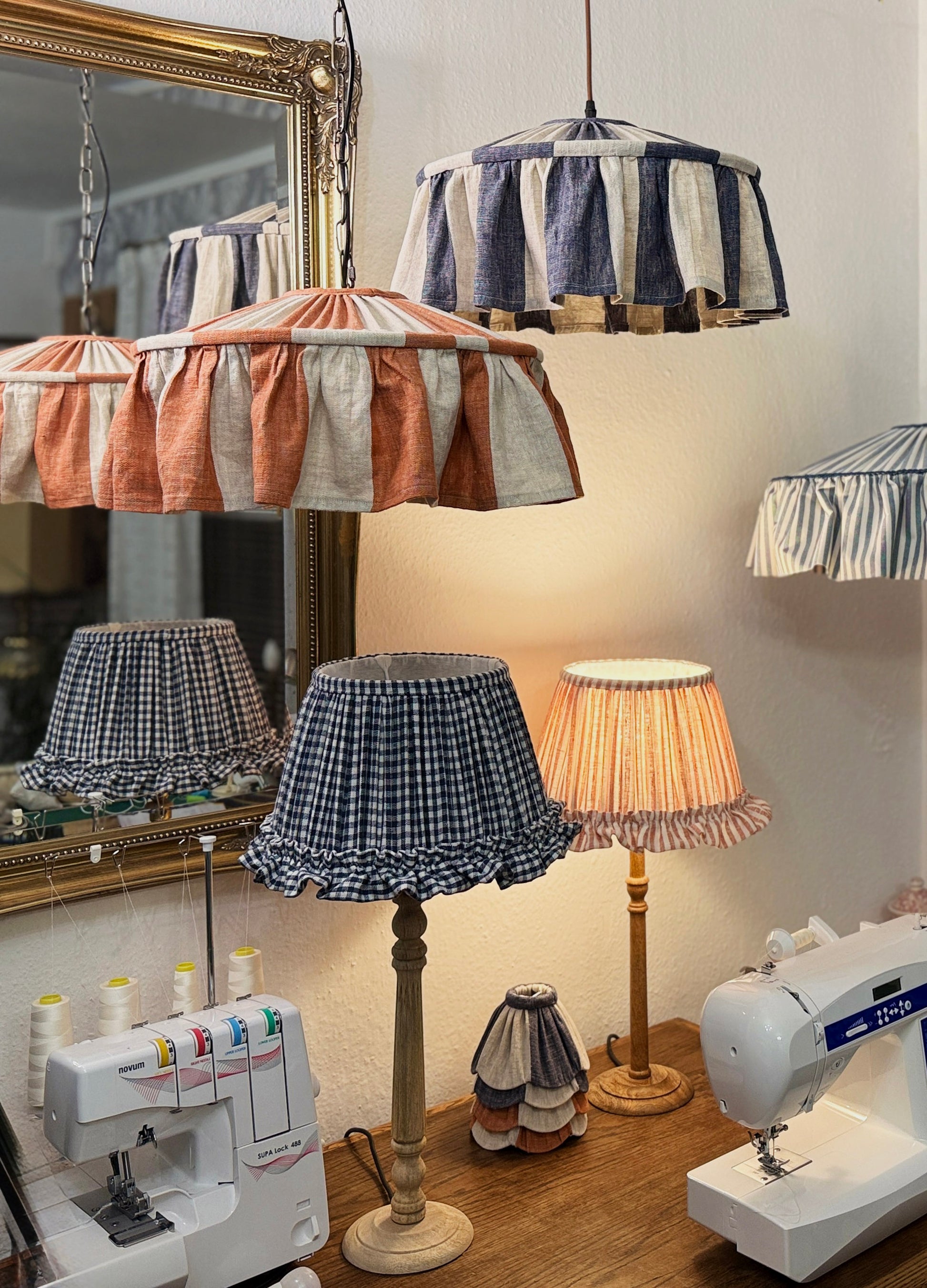 Various lampshades on a table with sewing machines in a workshop setting.