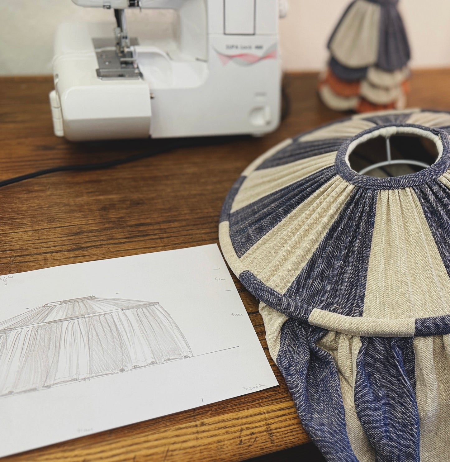 Fabric lampshade on a wooden table with a sewing machine and pattern paper in the background