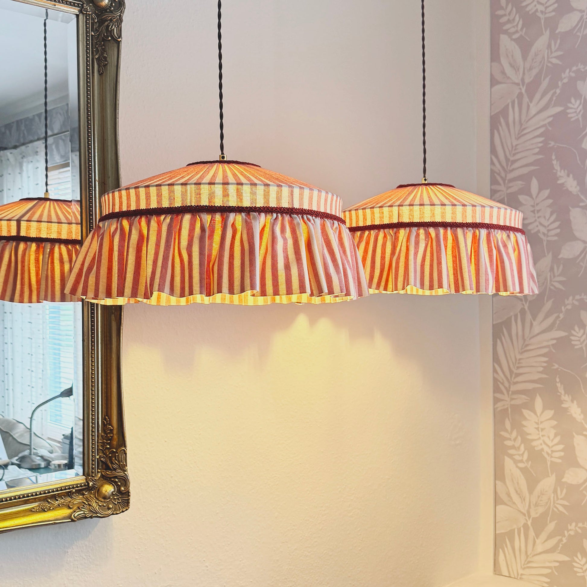 Striped pendant lights hanging in a room with a decorative mirror and leafy pattern.
