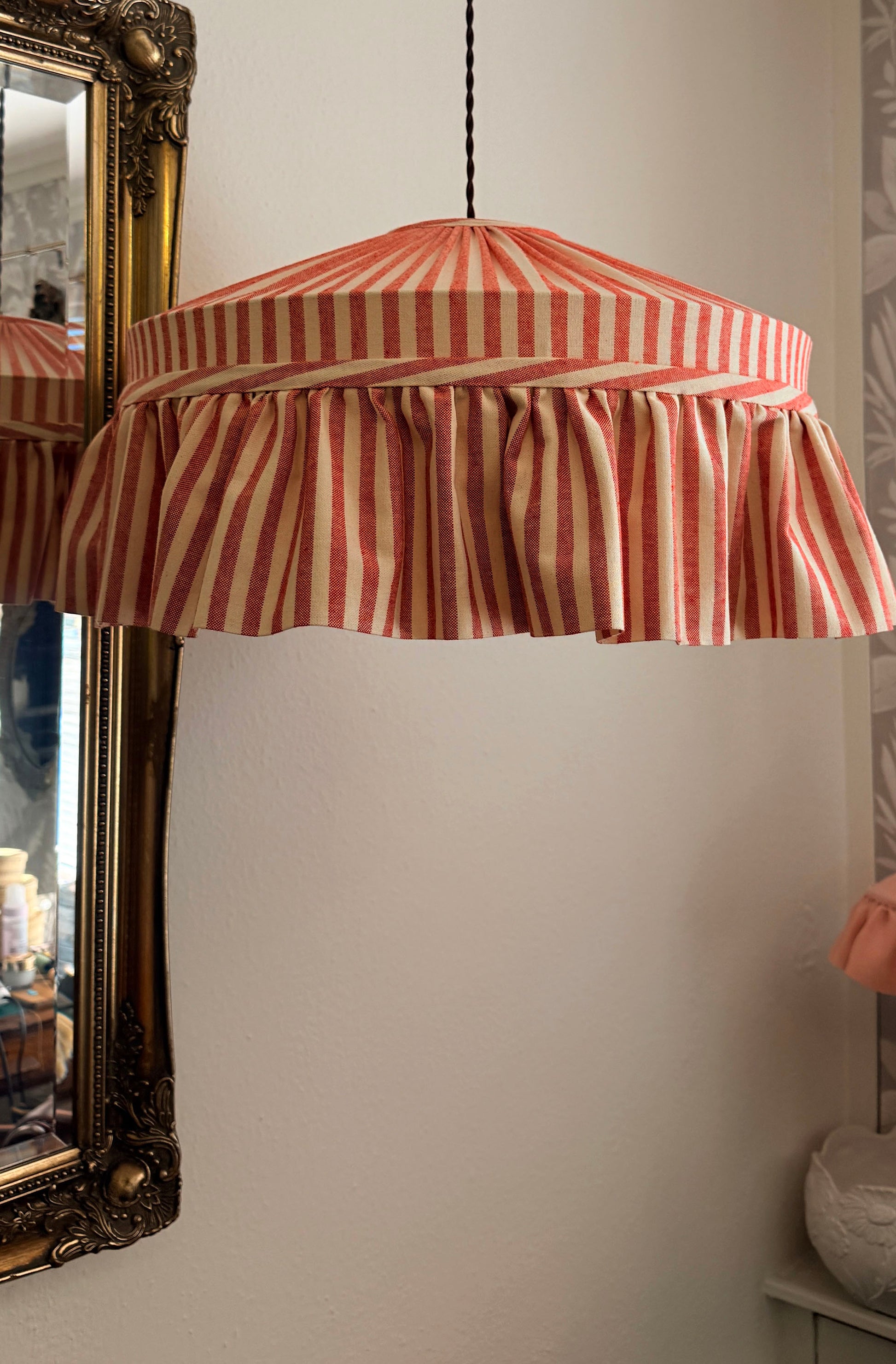 Striped lampshade hanging above a mirror with decorative frame.