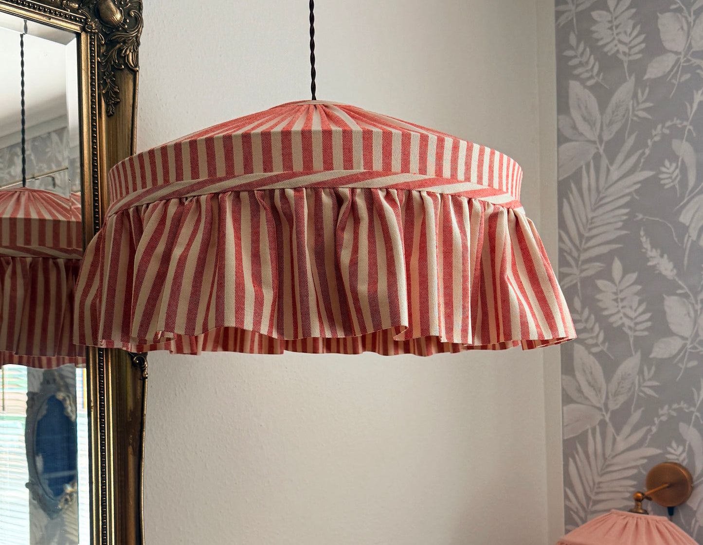 Striped lampshade hanging in a room with floral wallpaper