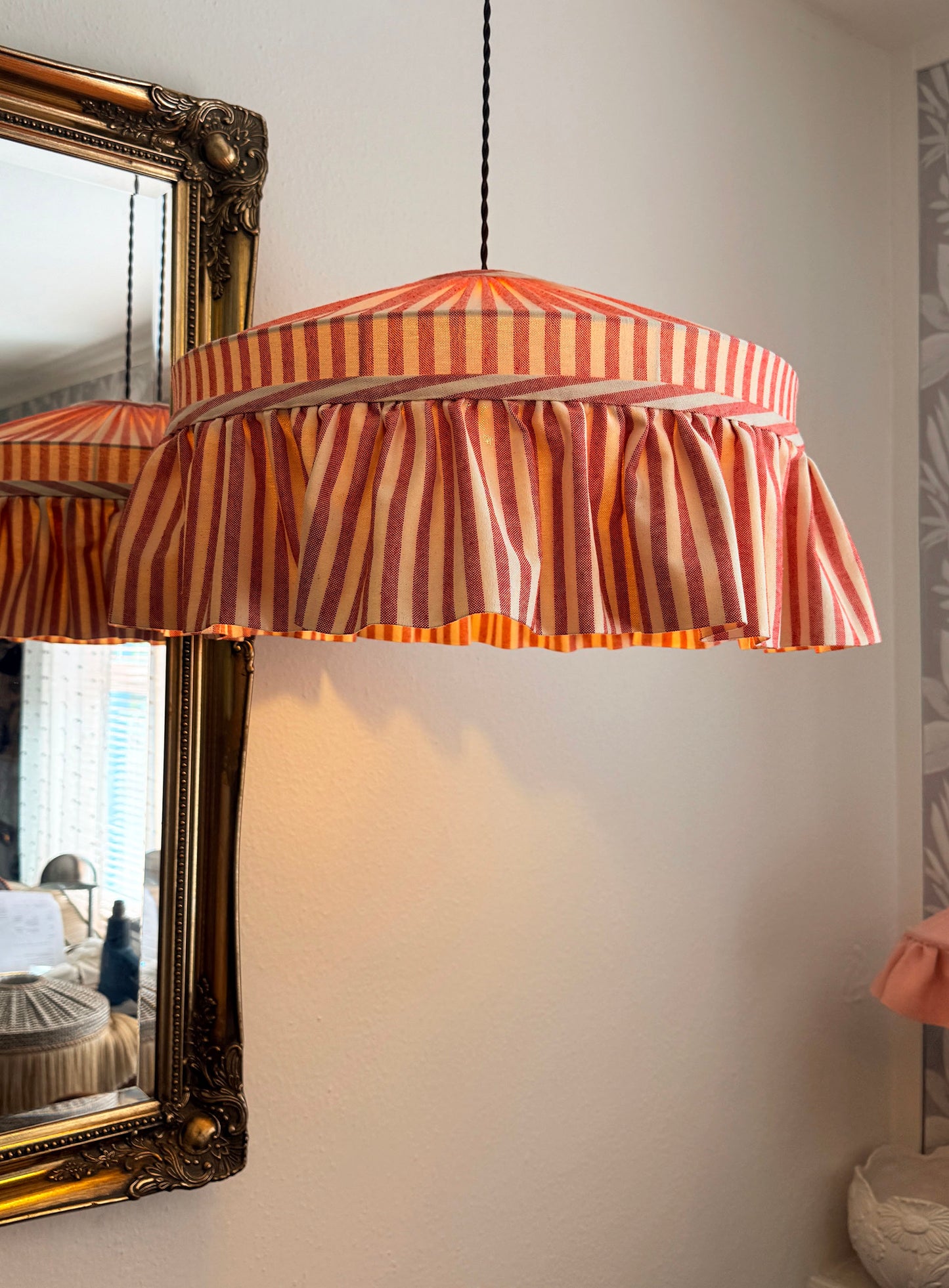 Striped lampshade hanging in a room with a mirror and decorative elements.