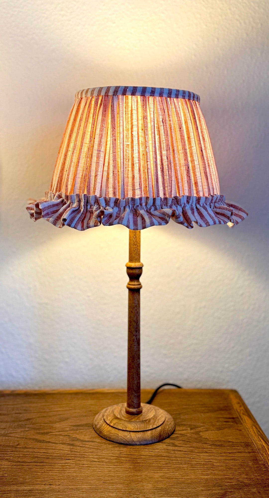 Table lamp with a pleated lampshade on a wooden surface. Maria Marabella Shades