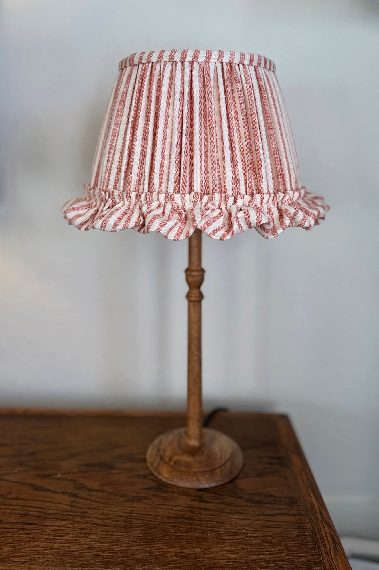 Lamp with a red and white striped shade on a wooden base against a plain background