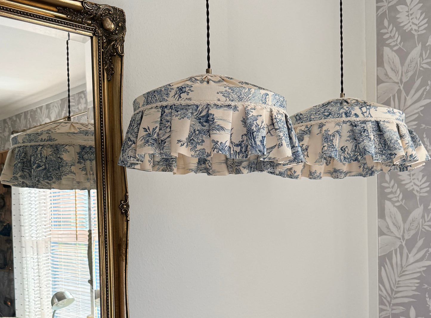 Fabric-covered pendant lights hanging in a room with a mirror and floral wallpaper.