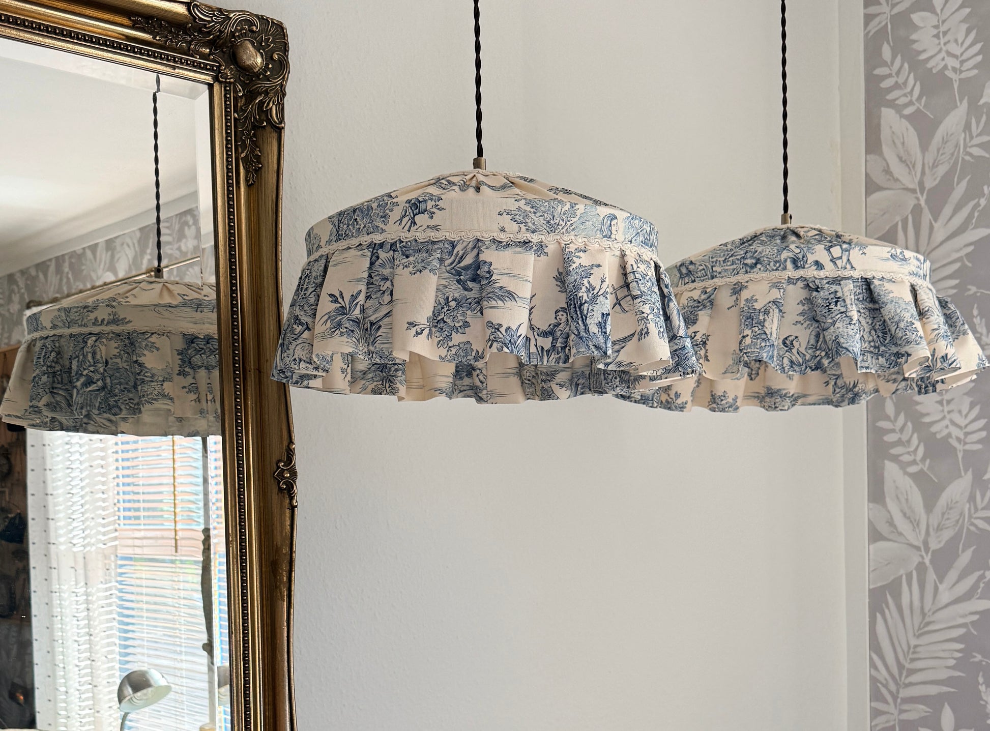 Fabric-covered pendant lights hanging in a room with a mirror and floral wallpaper.