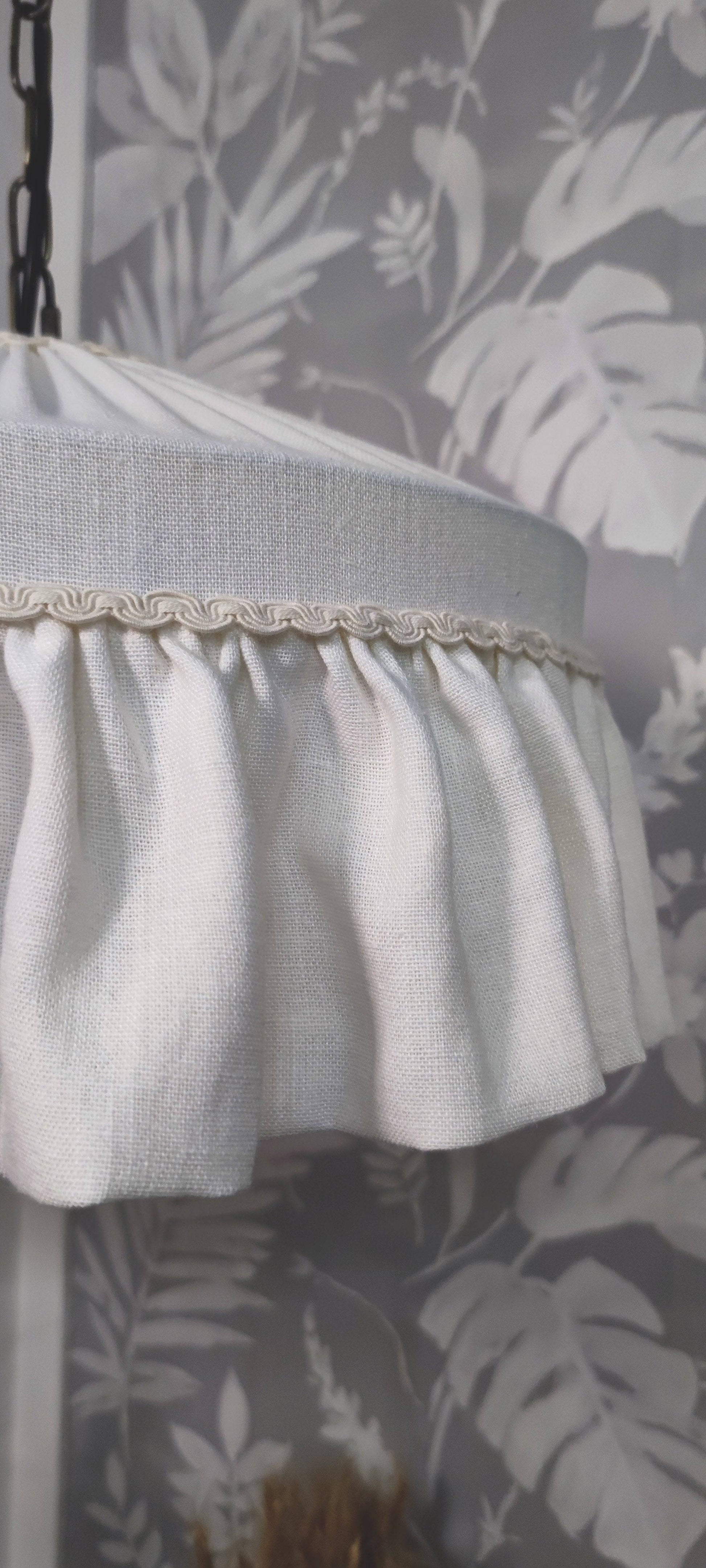 White skirt with lace trim lampshade  against a leaf-patterned wall.