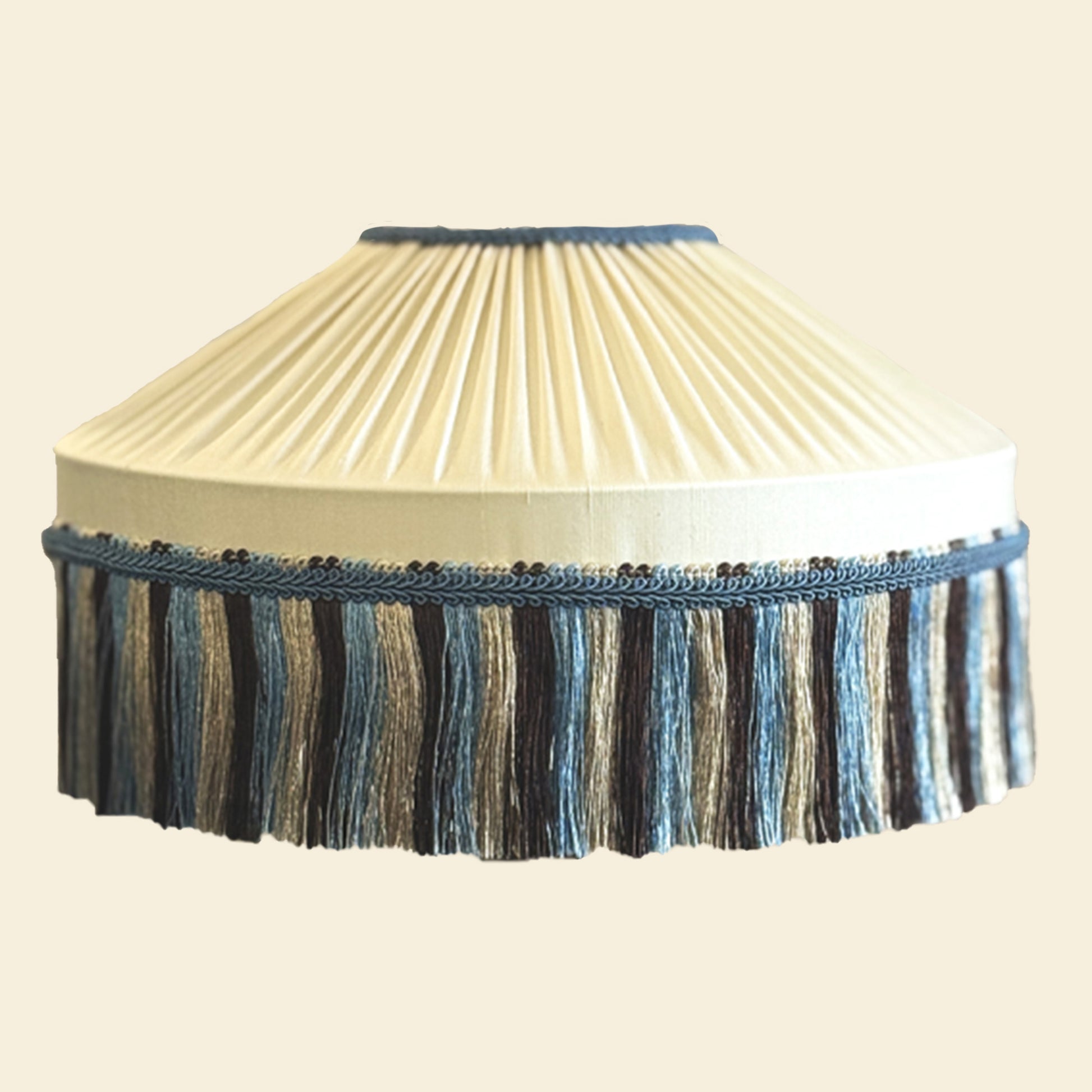 Decorative lampshade with pleated design and blue fringe on a beige background