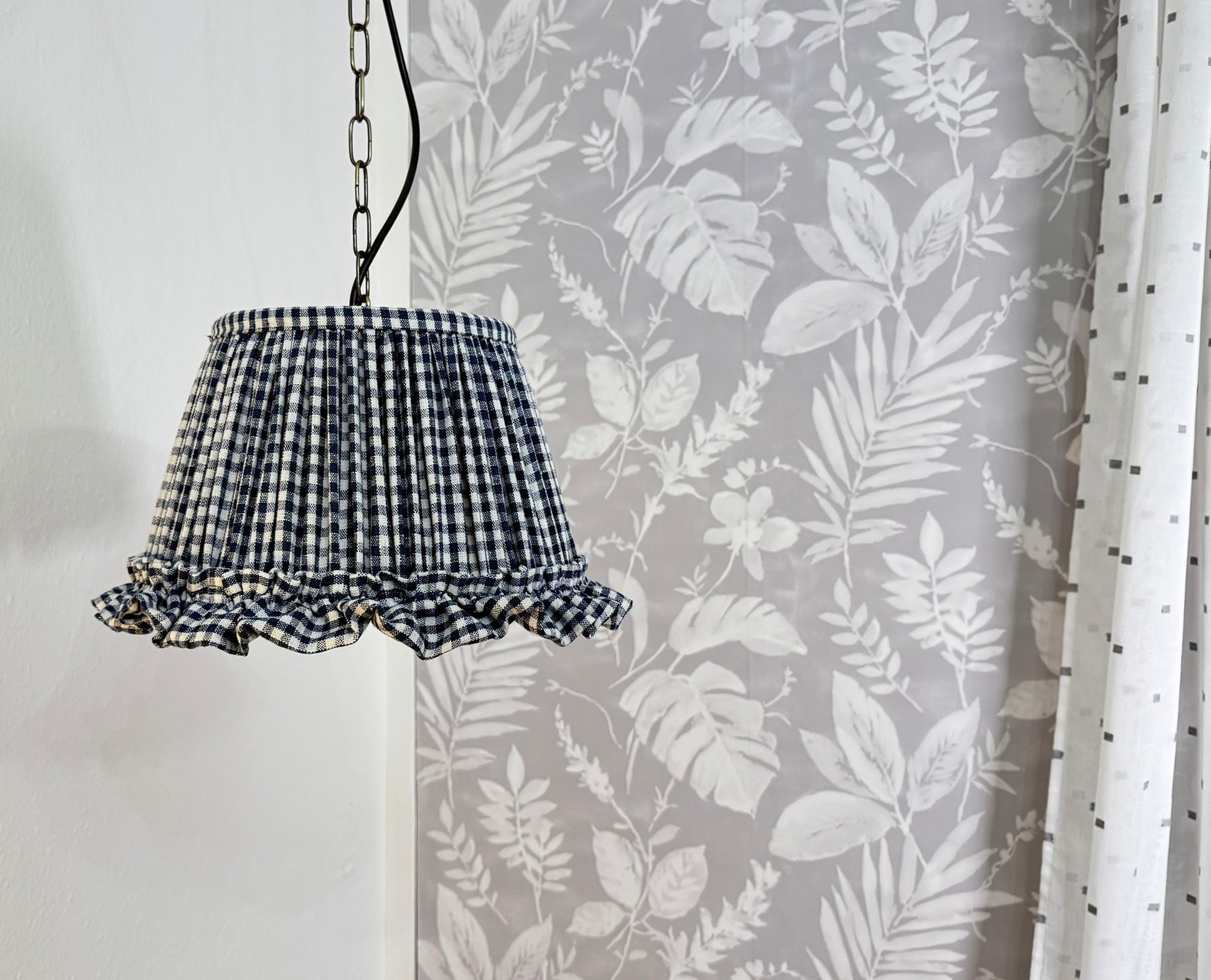 Indigo and white checkered lampshade hanging against a floral curtain background