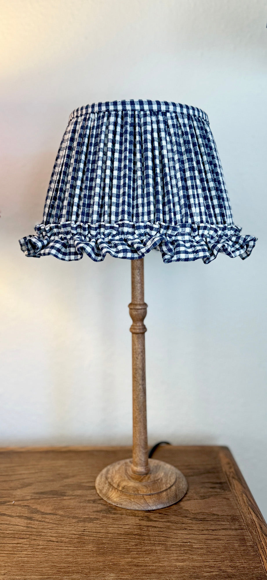 Lamp with a blue and white checkered lampshade on a wooden base against a white wall.