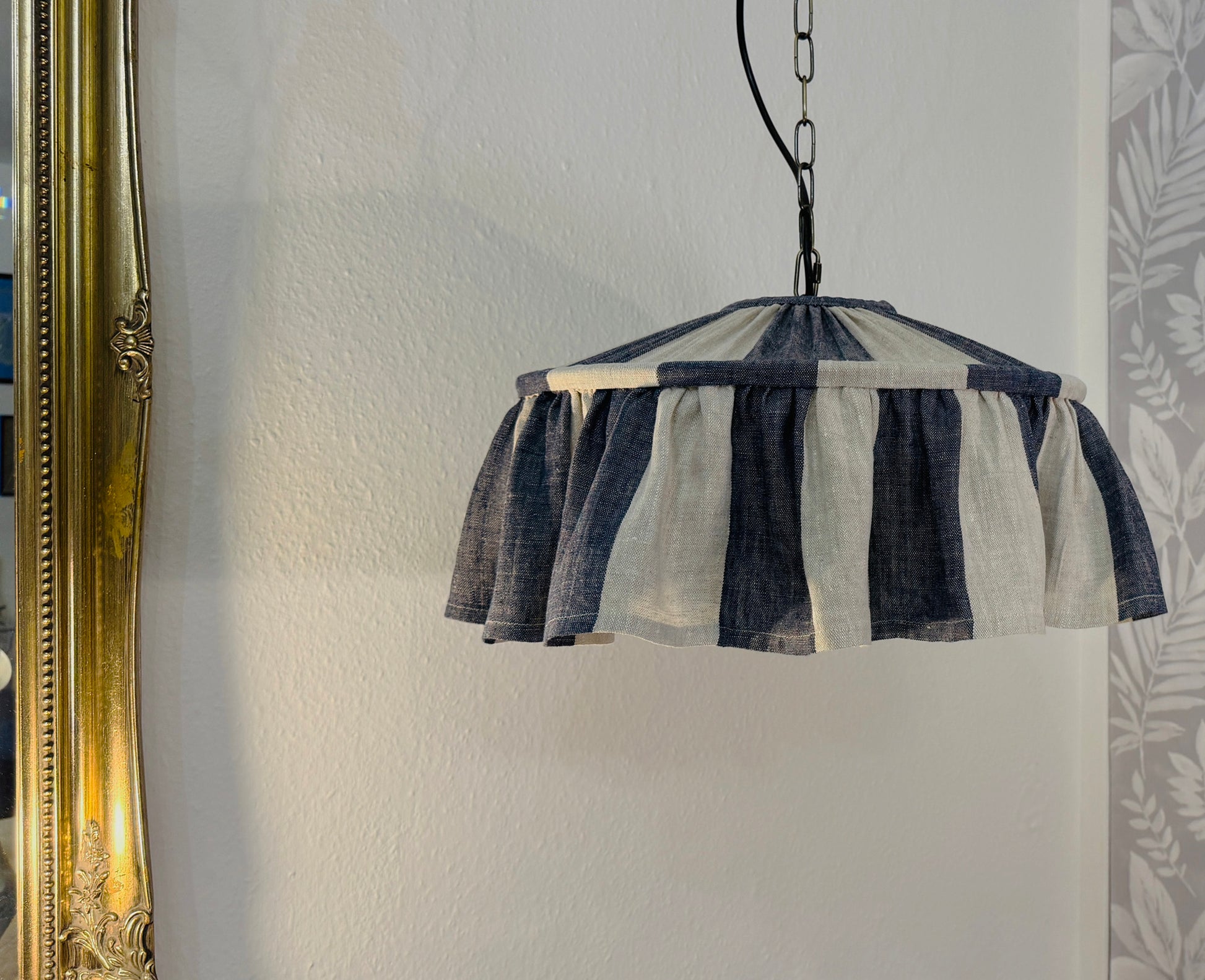 Striped indigo lampshade hanging on a wall with a decorative mirror and leaf pattern.