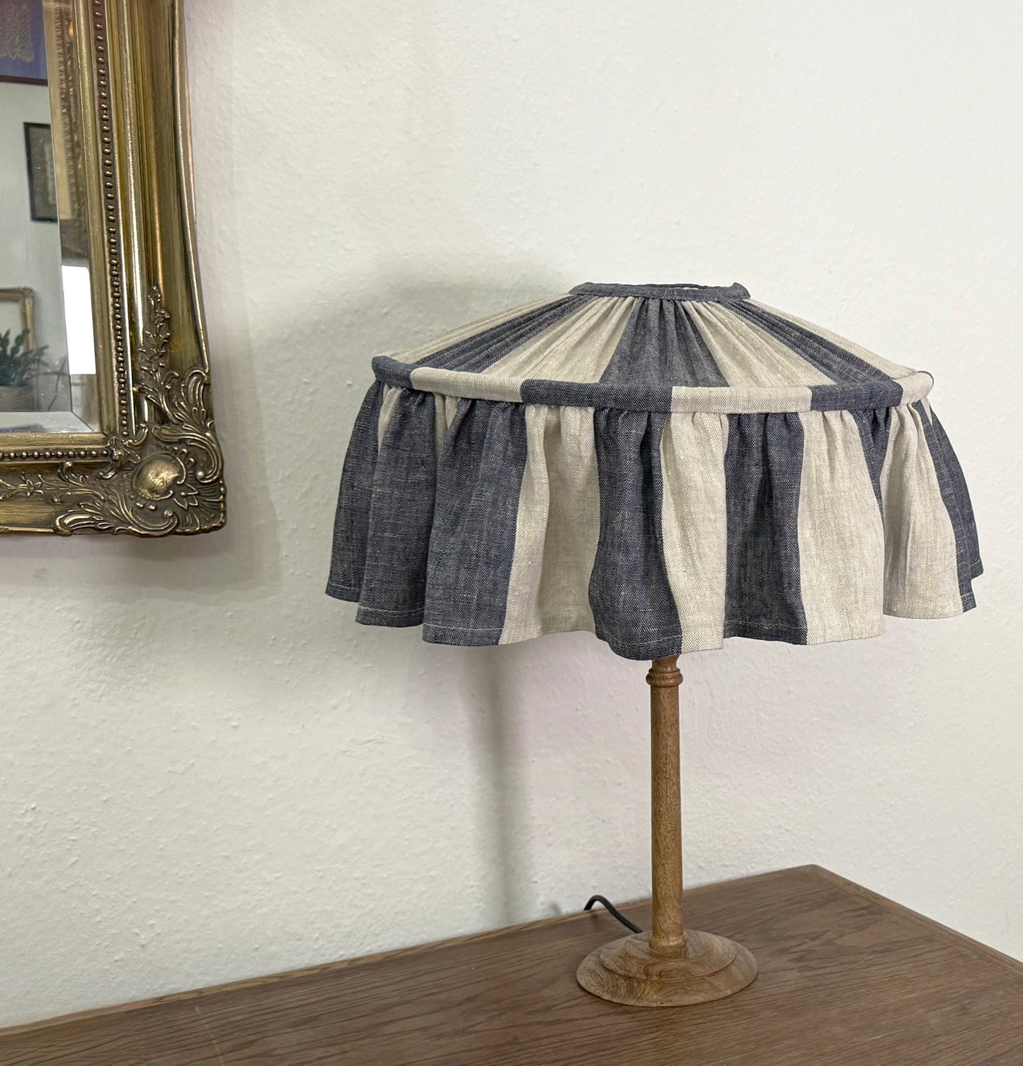 Table lamp with a striped fabric shade on a wooden base against a white wall.