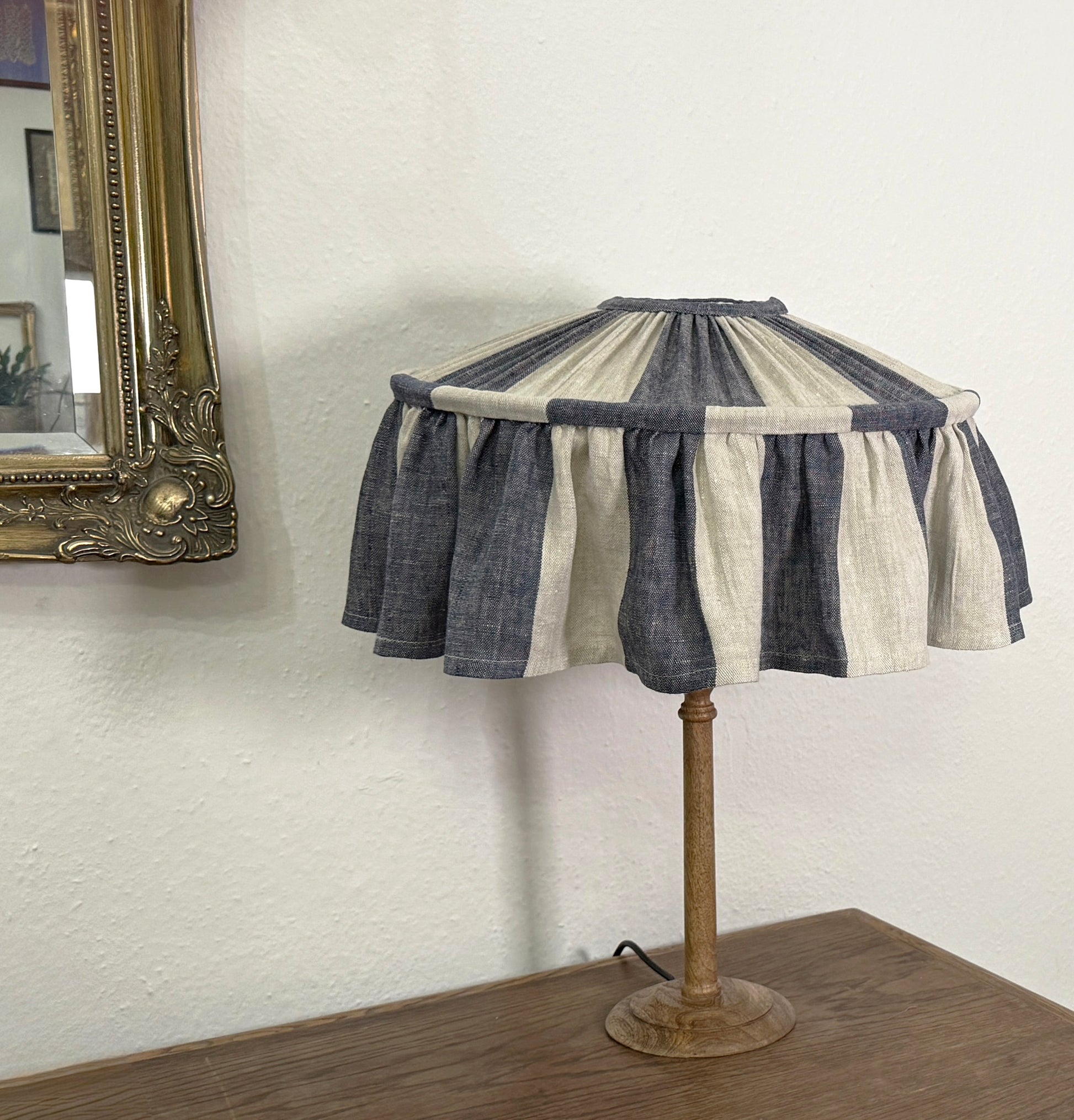 Table lamp with a striped fabric shade on a wooden base against a white wall.
