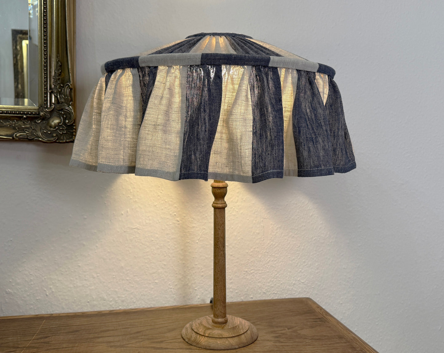 Table lamp with a striped indigo ruffle  lampshade on a wooden base against a white wall.