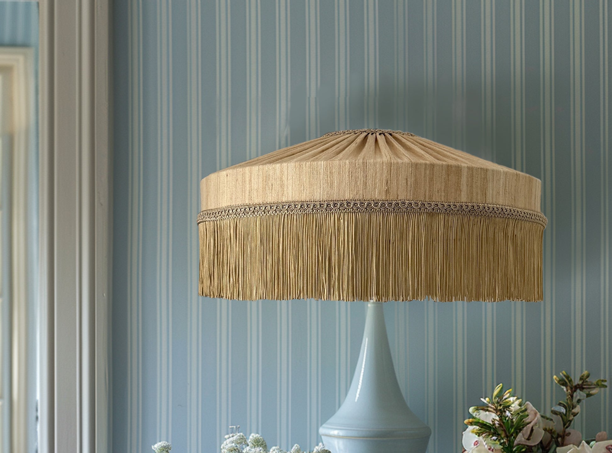 Lamp with a beige fringed shade against a striped blue wall