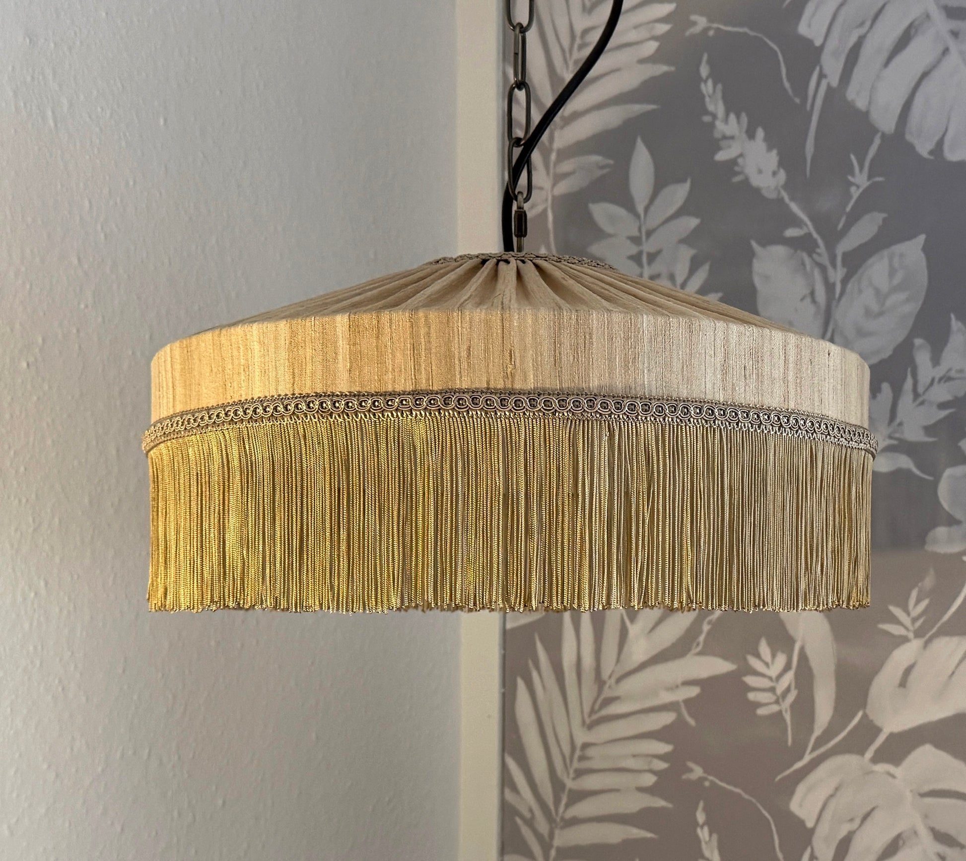 Pendant light with gold fringe shade against a floral wallpaper background